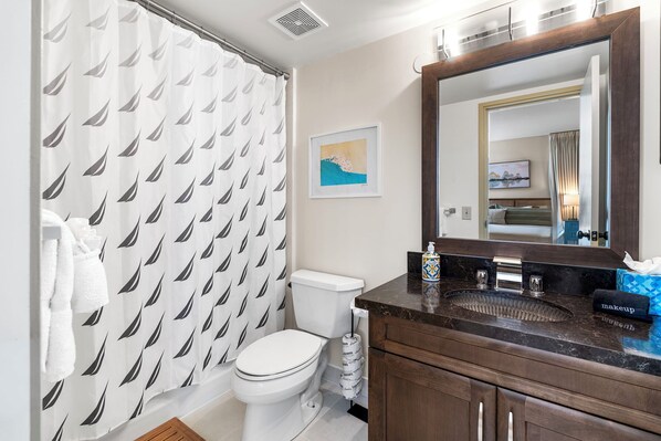 Un baño con inodoro, lavabo, espejo y cortina de ducha estampada con hojas.