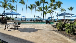 A poolside area with lounge chairs, umbrellas, and palm trees.