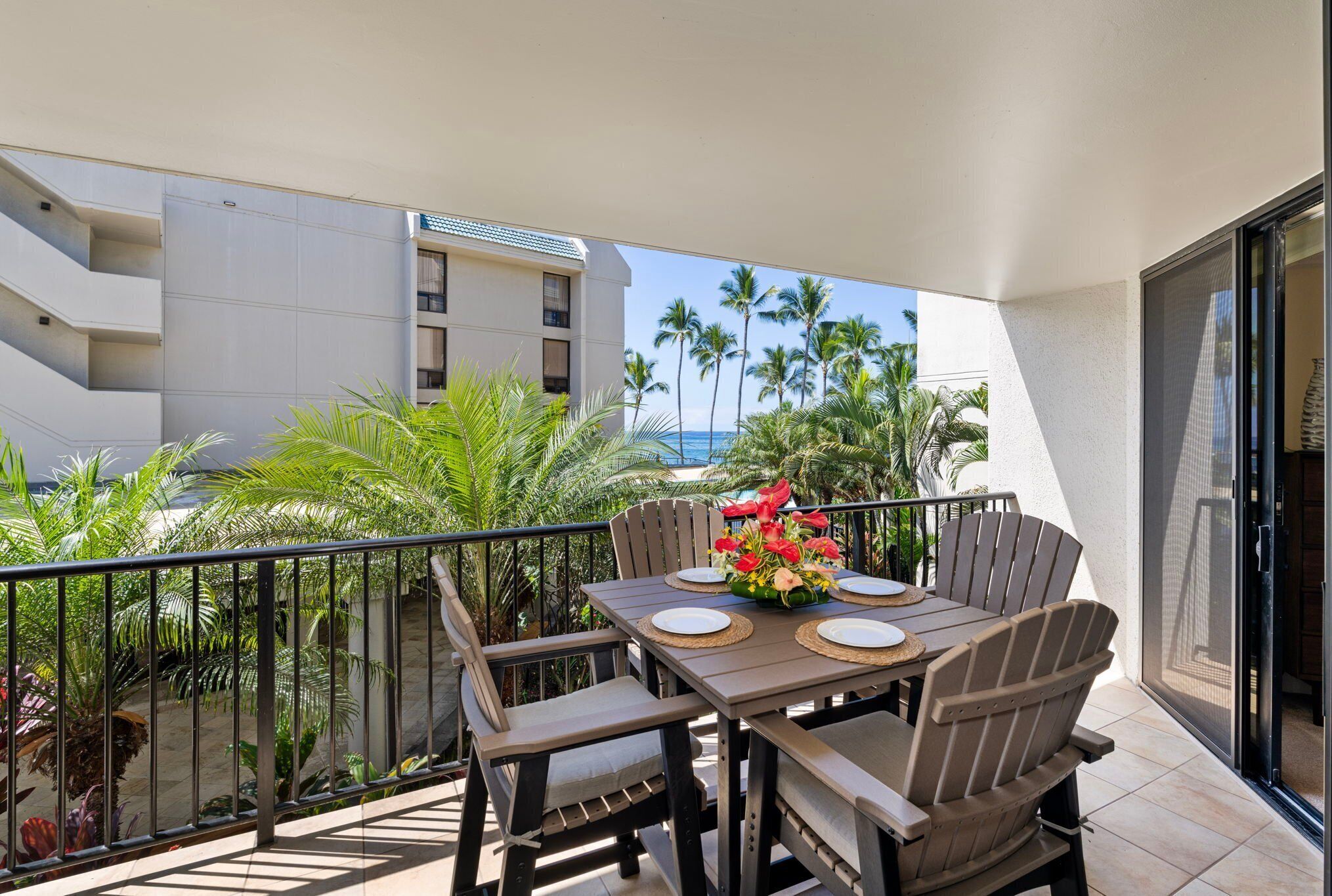 A balcony with a table set for two, surrounded by chairs, overlooking a pool and palm trees.