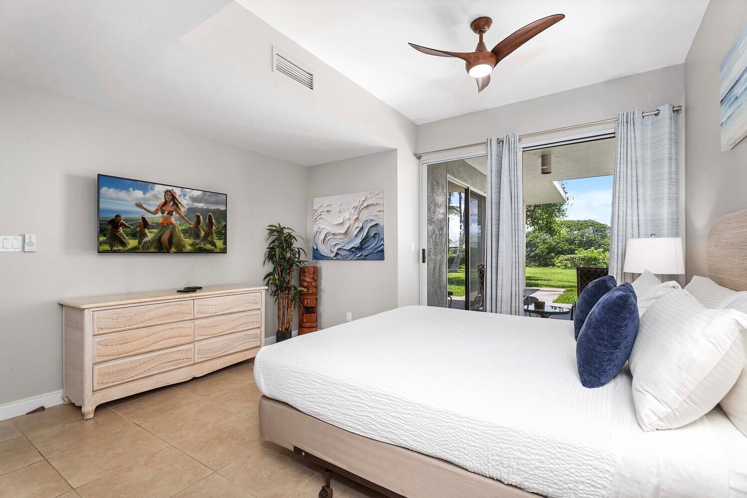 A bedroom with a bed, a dresser, a ceiling fan, a TV, and a painting.