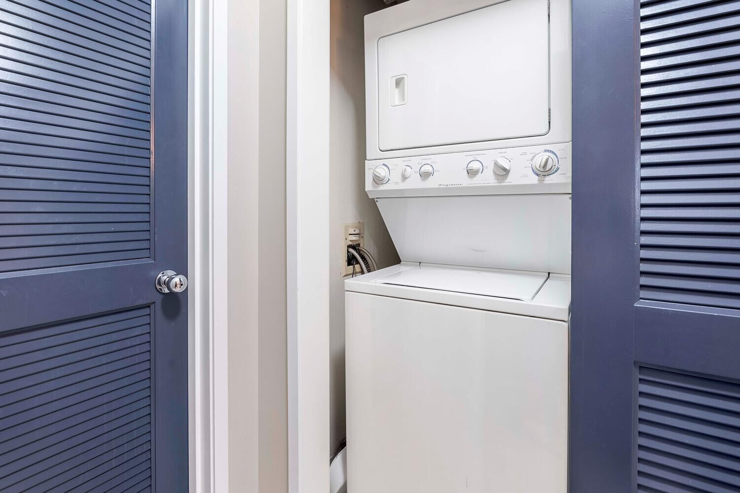 A laundry room with a white washer and dryer, a door with a handle, and a vent on the wall.