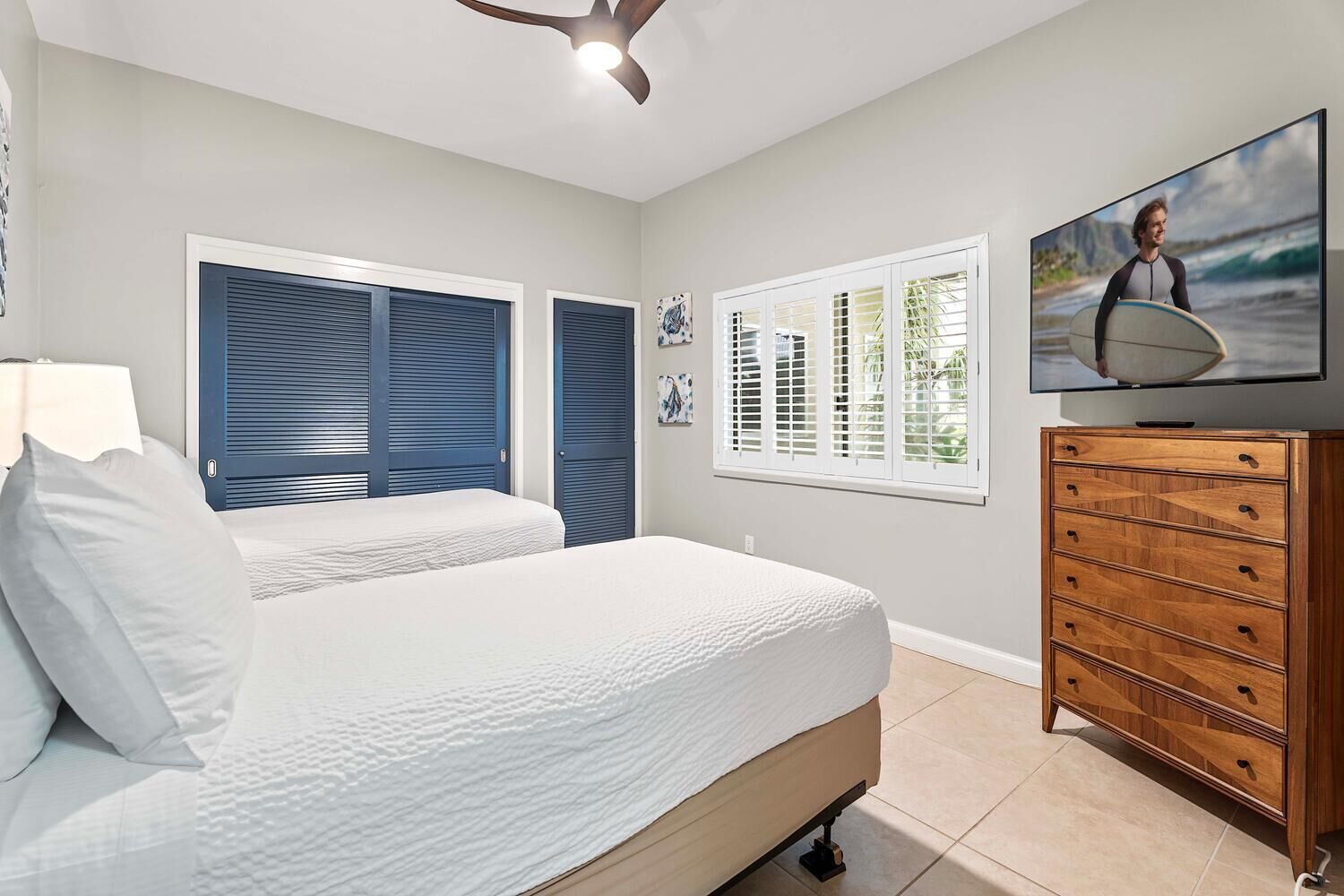 Une chambre à coucher avec un lit, une commode, un ventilateur de plafond et un téléviseur fixé au mur.