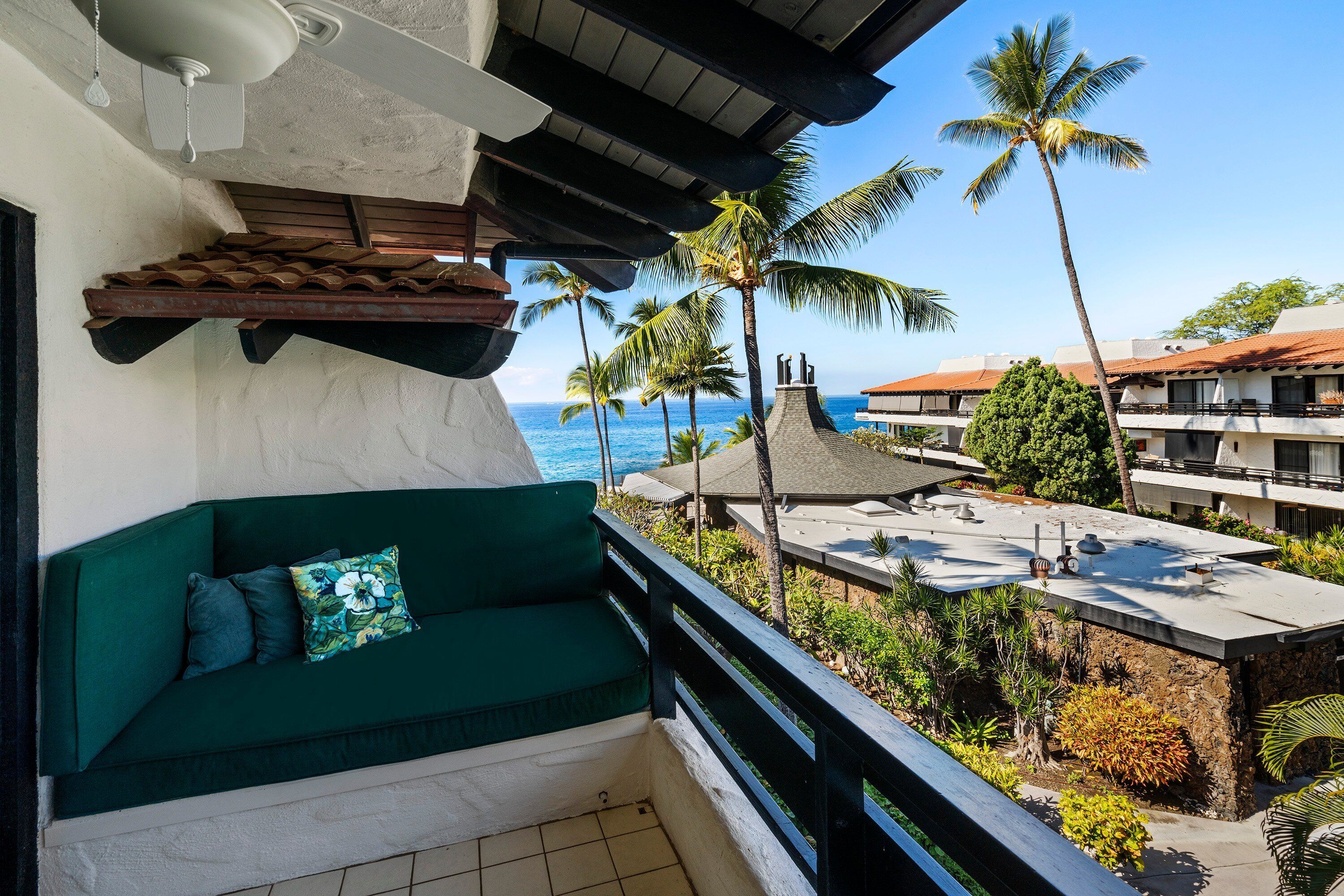 A balcony with a green sofa and a view of the ocean and palm trees.
