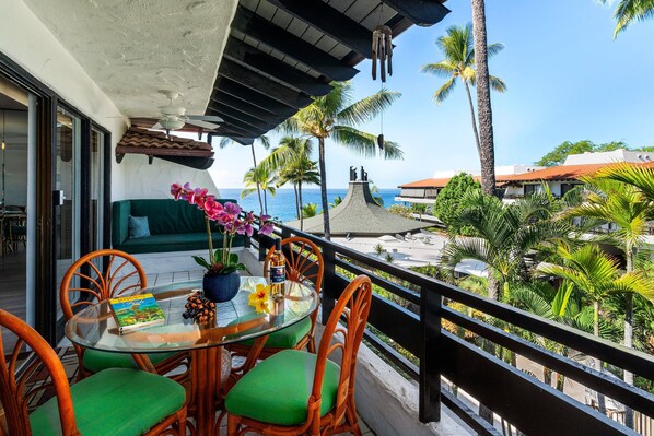A balcony with a glass table, wicker chairs, and a view of the ocean. - Quiet Complex - AC & Wifi - Well-equipped - Vrkcv (Kailua-Kona)