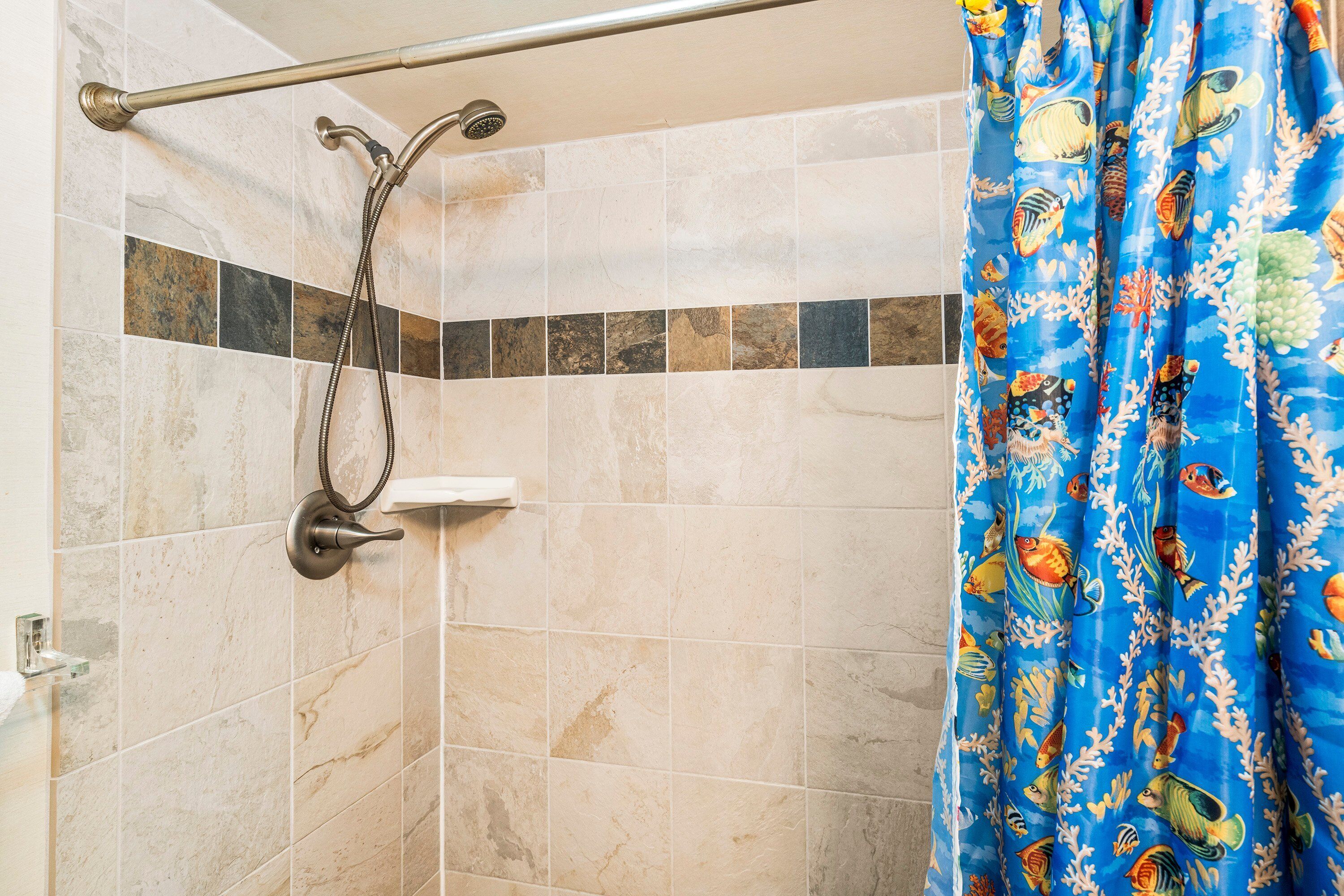 A shower area with a hand shower, a glass shelf, and a tiled wall with a decorative tile border.