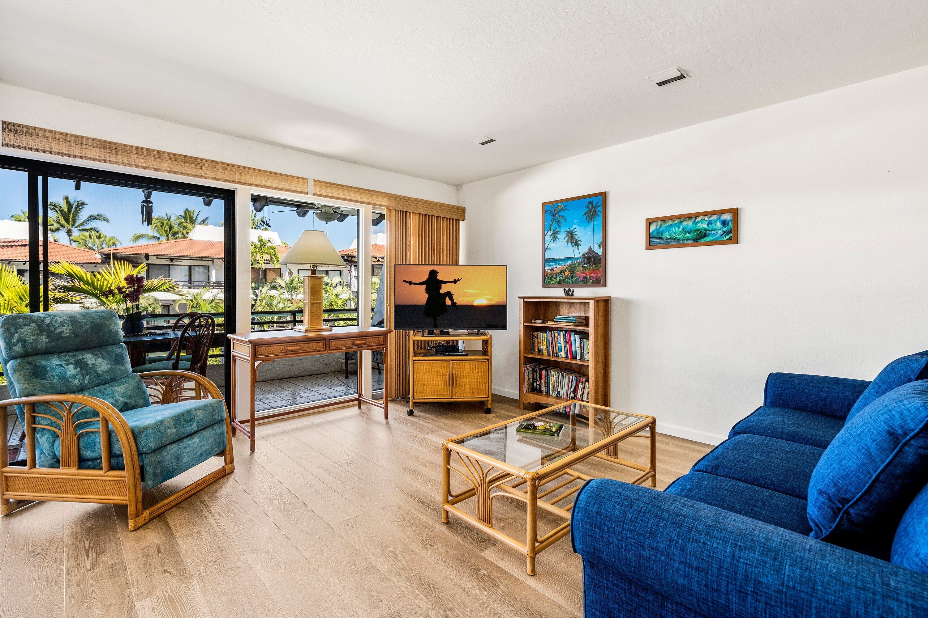 Un amplio salón con un gran ventanal, un sofá azul, una mesa de centro de madera, un televisor y una estantería.