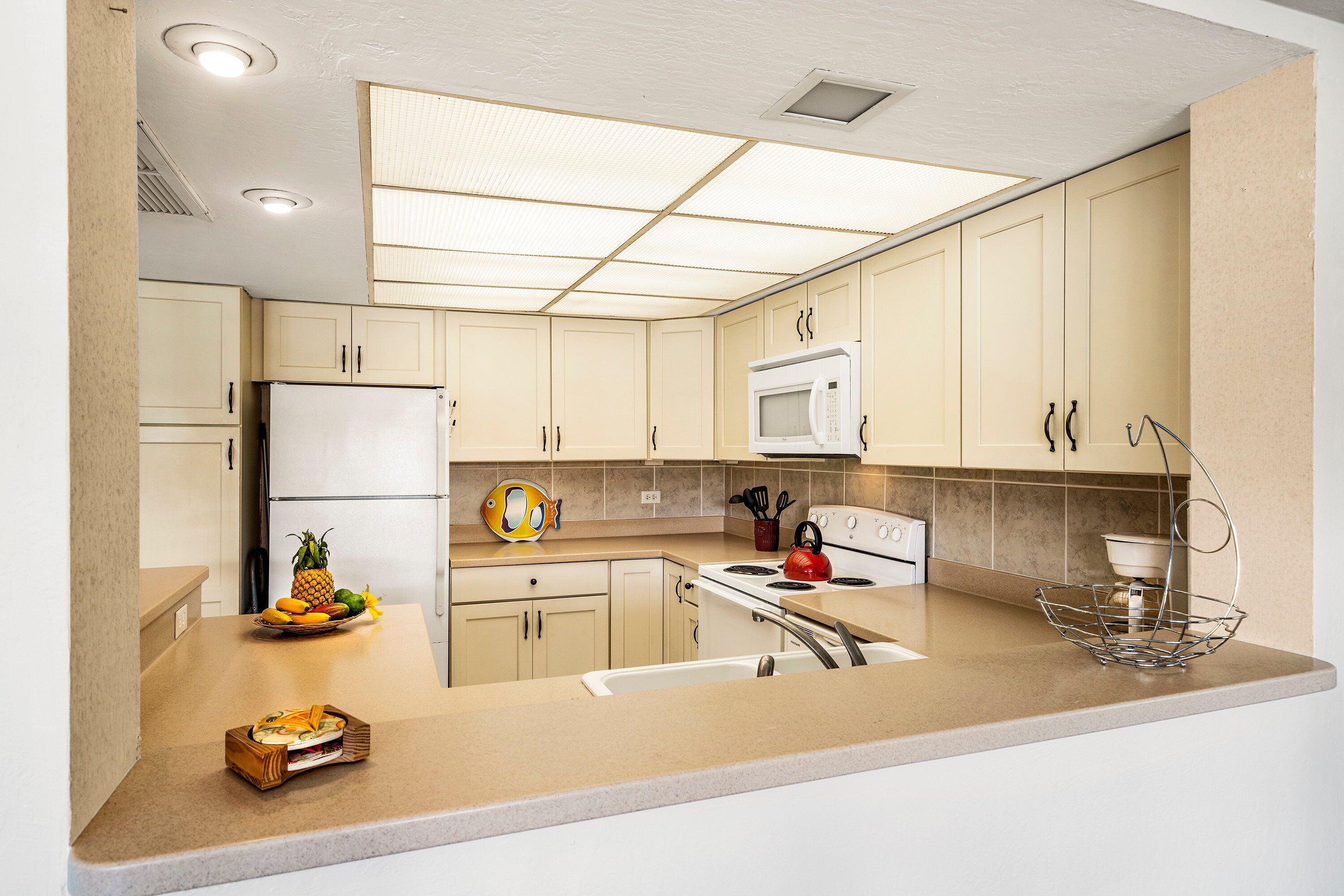 A modern kitchen with beige cabinets, a stainless steel refrigerator, a microwave, and a gas stove.