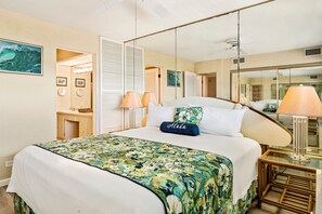 A hotel room with a bed, a mirror, a bedside table with a lamp, and a view of the sea through the window. - Quiet Complex - AC & Wifi - Well-equipped - Vrkcv (Kailua-Kona)
