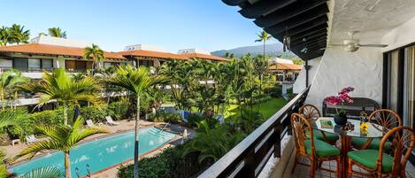 A balcony with a view of a swimming pool, surrounded by palm trees and a building with a tiled roof.