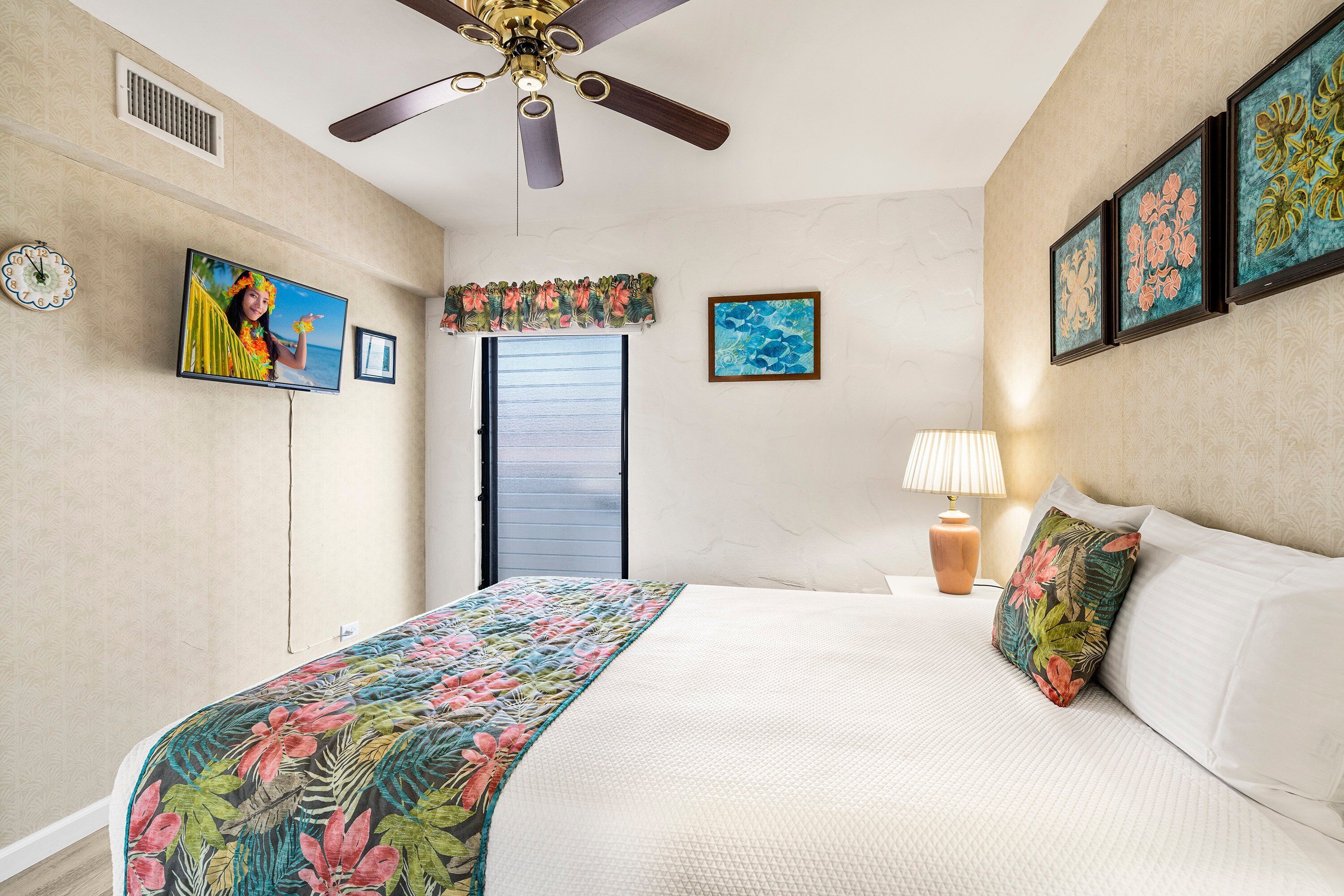 Une chambre à coucher avec un lit, un ventilateur de plafond, une fenêtre et des œuvres d’art murales.