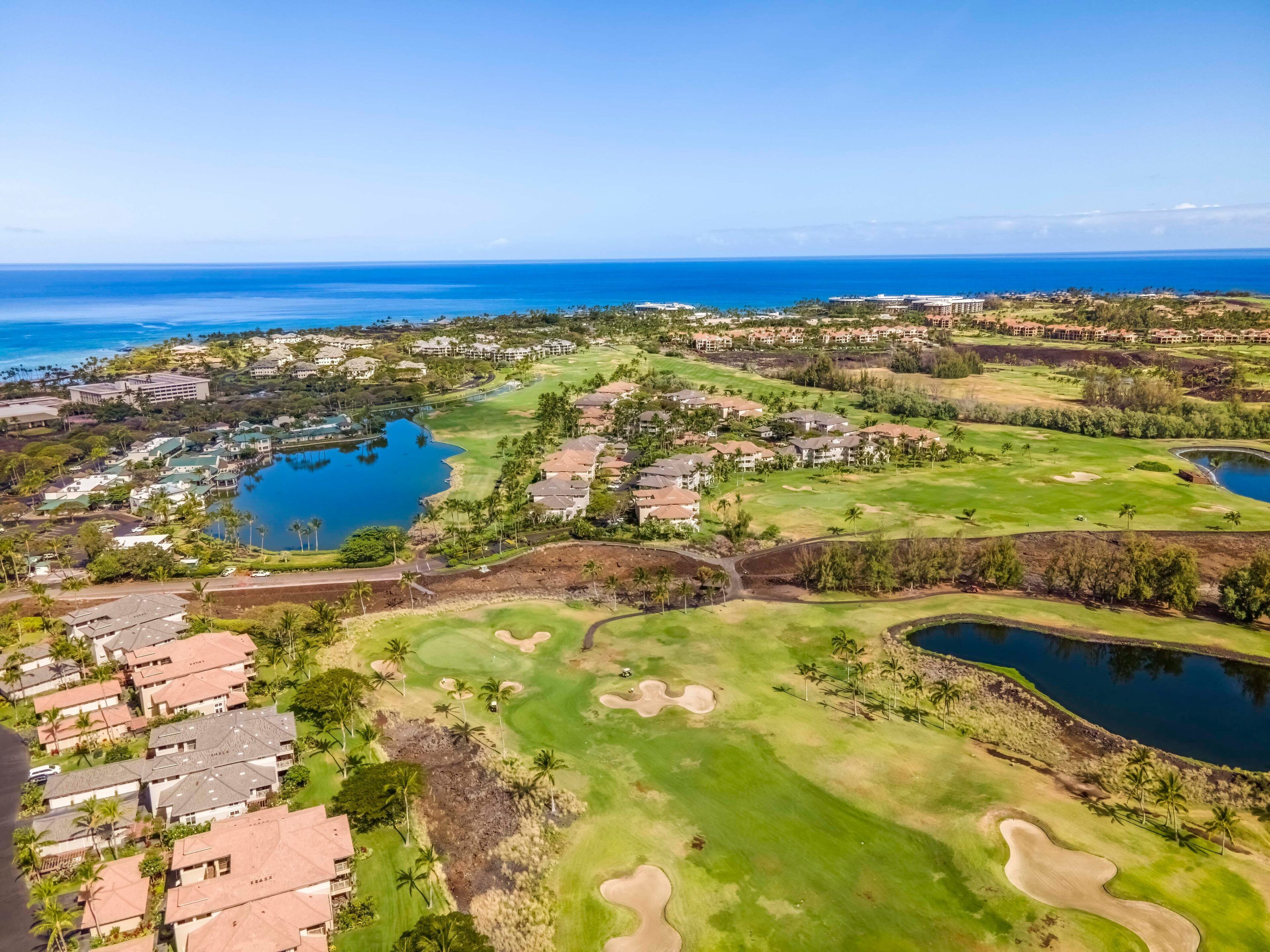 A golf course with multiple water bodies, residential areas, and a clear view of the ocean.