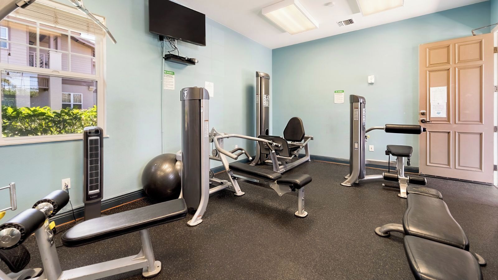 A gym with exercise equipment, a television, and a window with a view of buildings.
