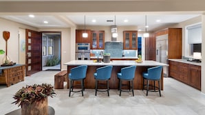 A modern kitchen with a large island, bar stools, wooden cabinets, and stainless steel appliances. - Unbelievable Ocean Front View w Pool - AC - Outdoor Seating!- Vrkcv (Kailua-Kona)