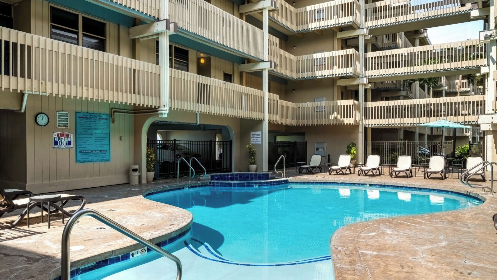A pool area with a blue pool, lounge chairs, and a multi-story building with balconies.
