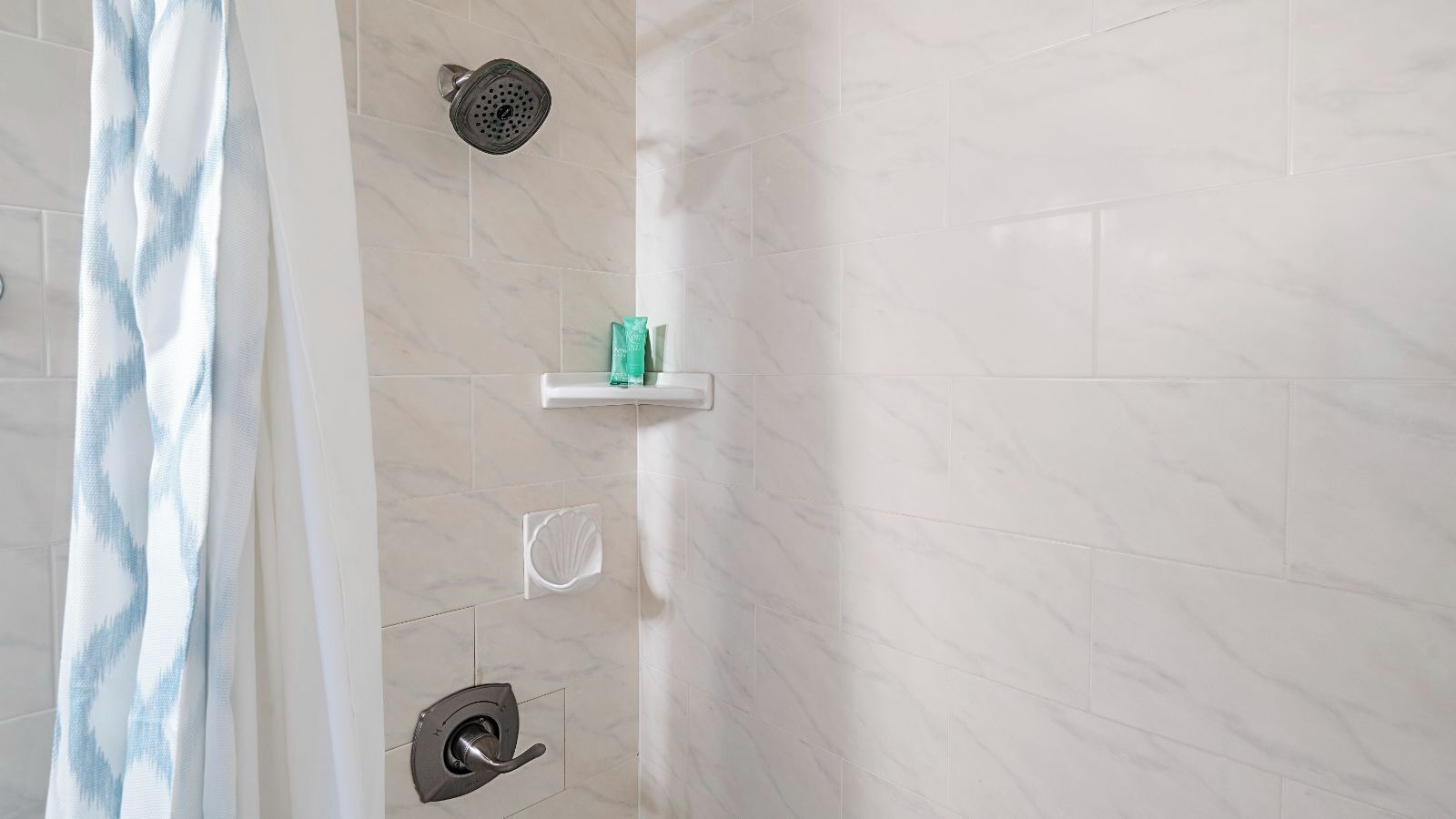 A shower area with a handheld showerhead, a soap dish, and a shower control panel.