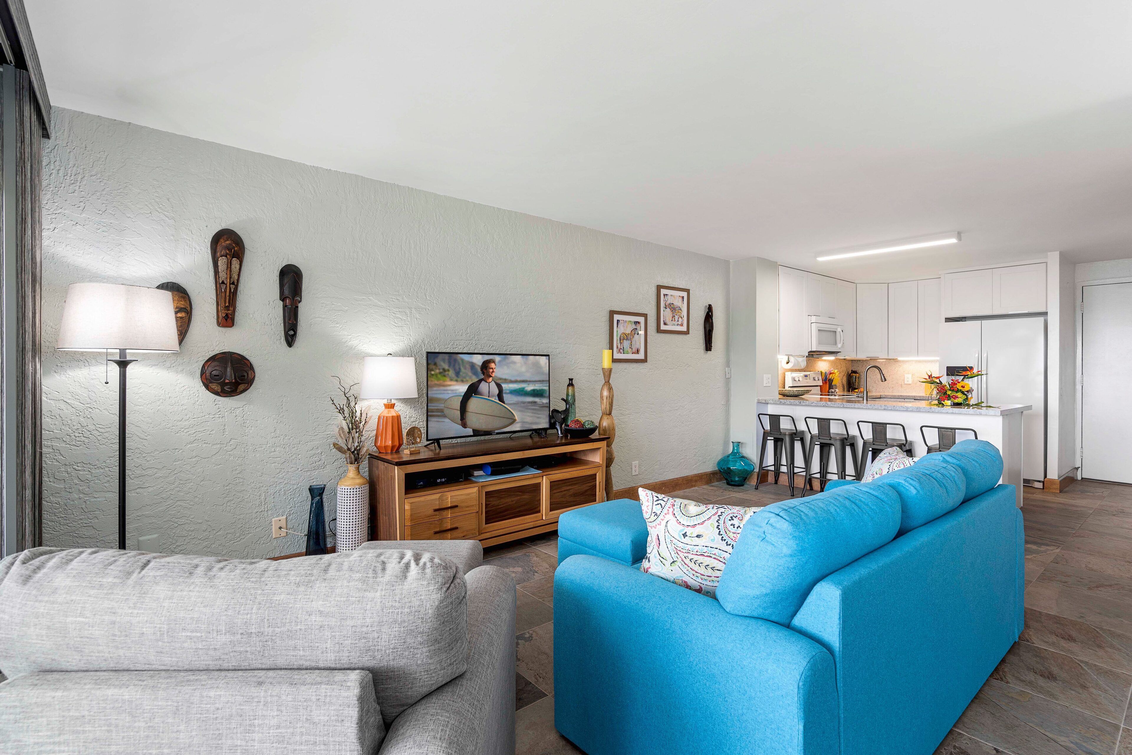 A modern living room with a grey sofa, a blue sofa, and a TV on a wooden stand.