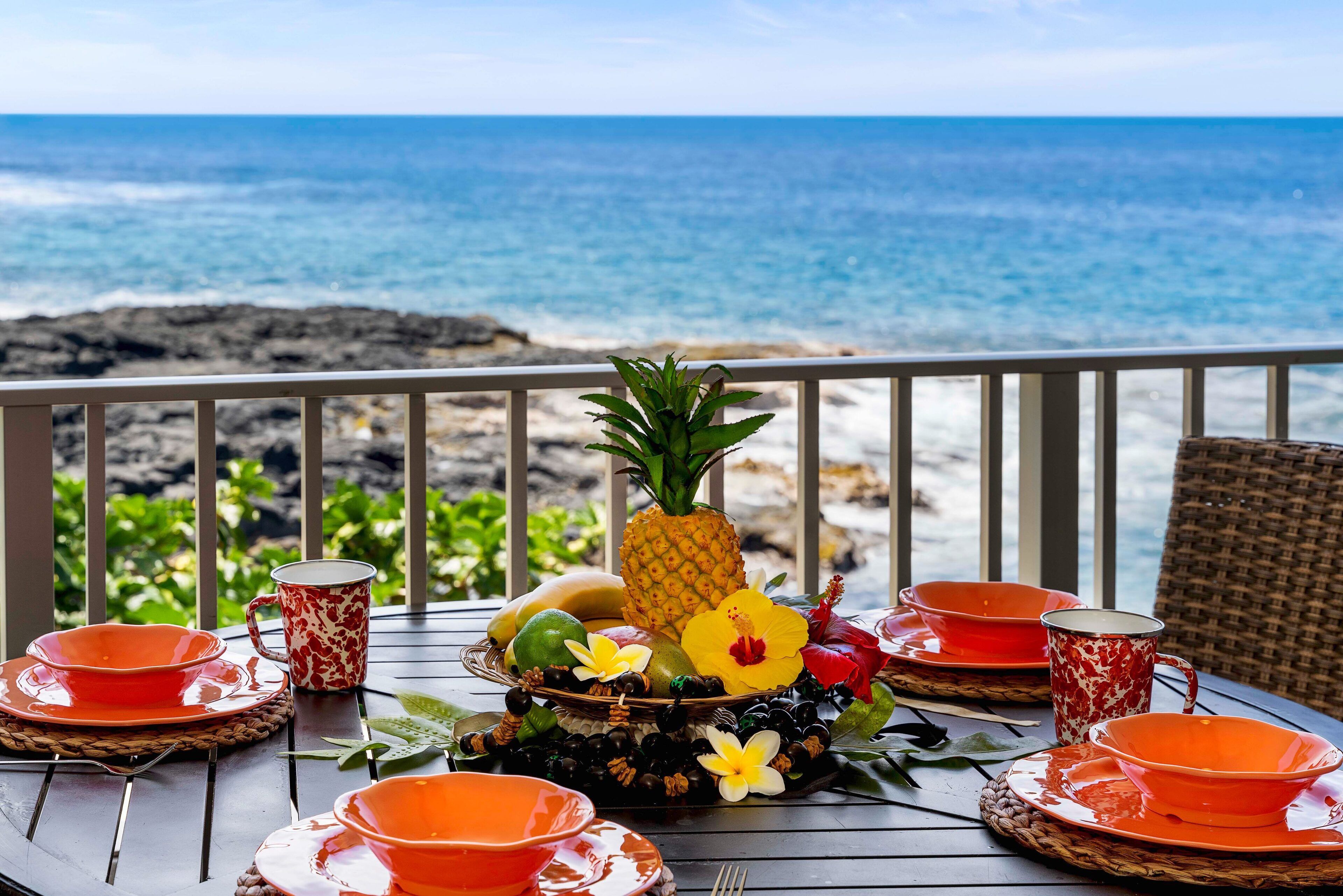 Une table dressée avec de la vaisselle orange et un centre de table en forme d’ananas, donnant sur une plage.