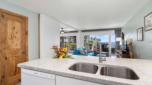A modern kitchen with a double sink, wooden cabinets, and a view to the living area. - Ocean Front Condo - Vrkcv (Kailua-Kona)