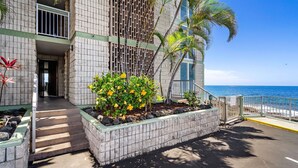 A building with a balcony, a staircase leading to the entrance, and a view of the ocean. - Ocean Front Condo - Vrkcv (Kailua-Kona)