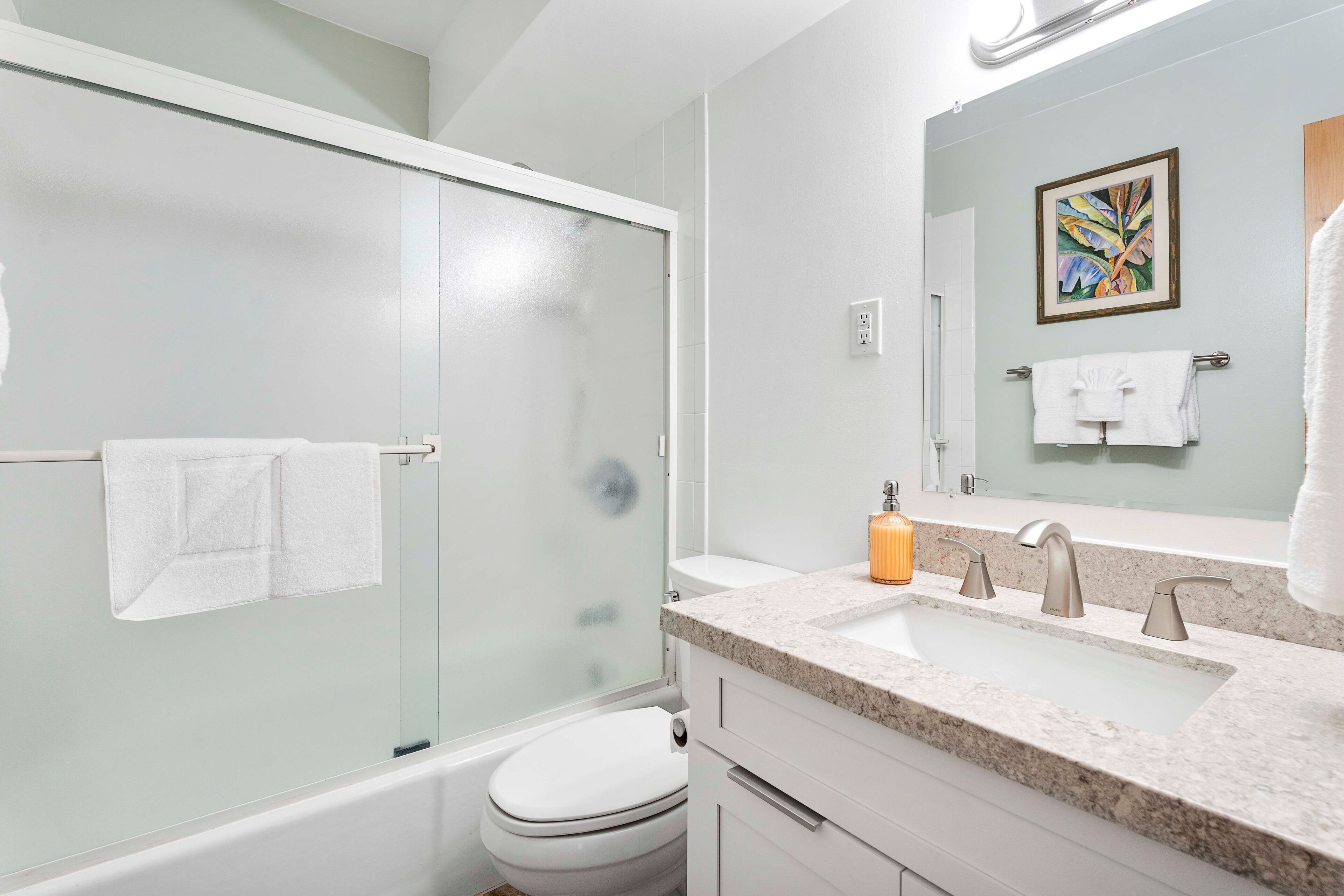 A modern bathroom with a glass-enclosed shower, a white toilet, a sink with a marble countertop, and a large mirror.