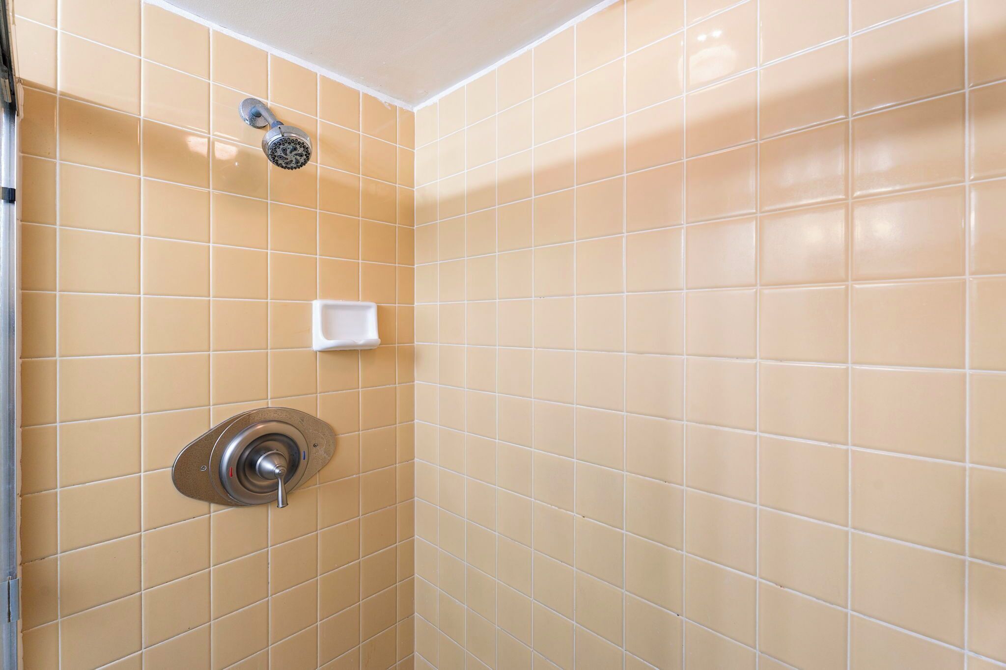 A bathroom with beige tiles, a showerhead, and a soap dish.