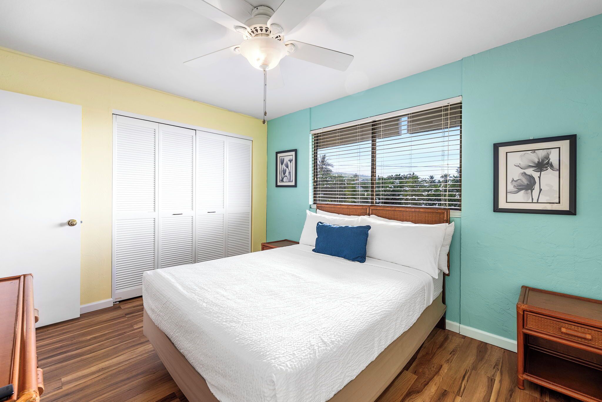 A bedroom with a bed, a ceiling fan, a window with blinds, and a door.