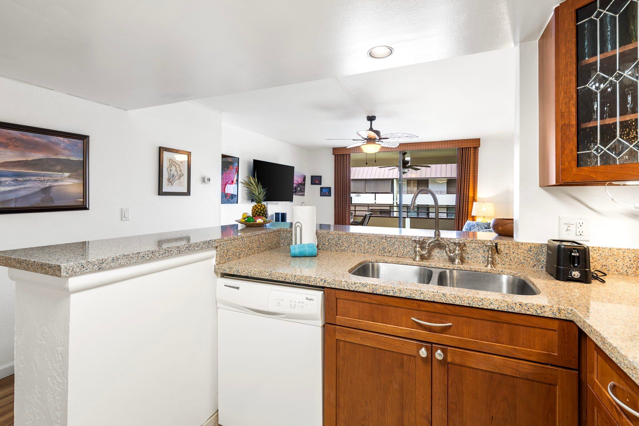 A modern kitchen with granite countertops, a dishwasher, wooden cabinets, a sink, and a ceiling fan.