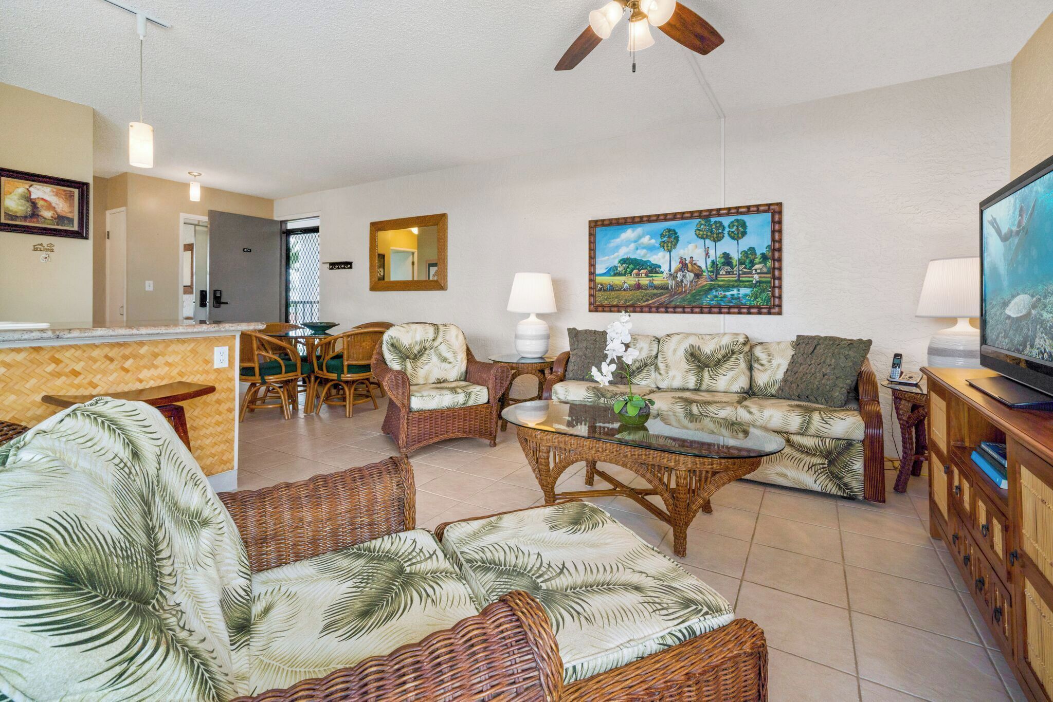 A living room with wicker furniture, a glass coffee table, and a television.