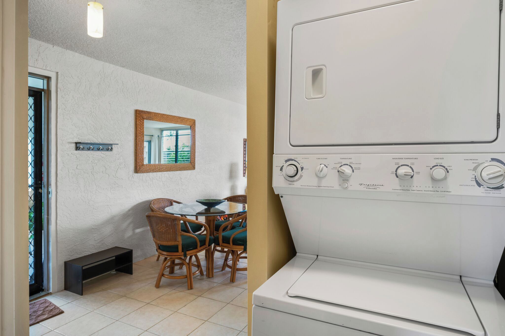 Un cuarto de lavandería con una lavadora blanca grande, una mesa pequeña con sillas y un espejo en la pared.