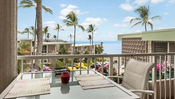 Un balcon avec une table, des chaises et une vue sur des palmiers et un bâtiment situé de l’autre côté de l’eau.