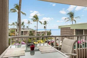 Een balkon met een tafel, stoelen en uitzicht op palmbomen en een gebouw aan de overkant van het water.