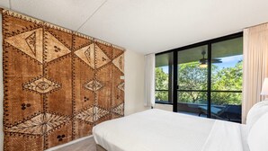 Une chambre d’hôtel avec un grand lit, une tapisserie à motifs sur le mur et une vue sur la verdure par la fenêtre.