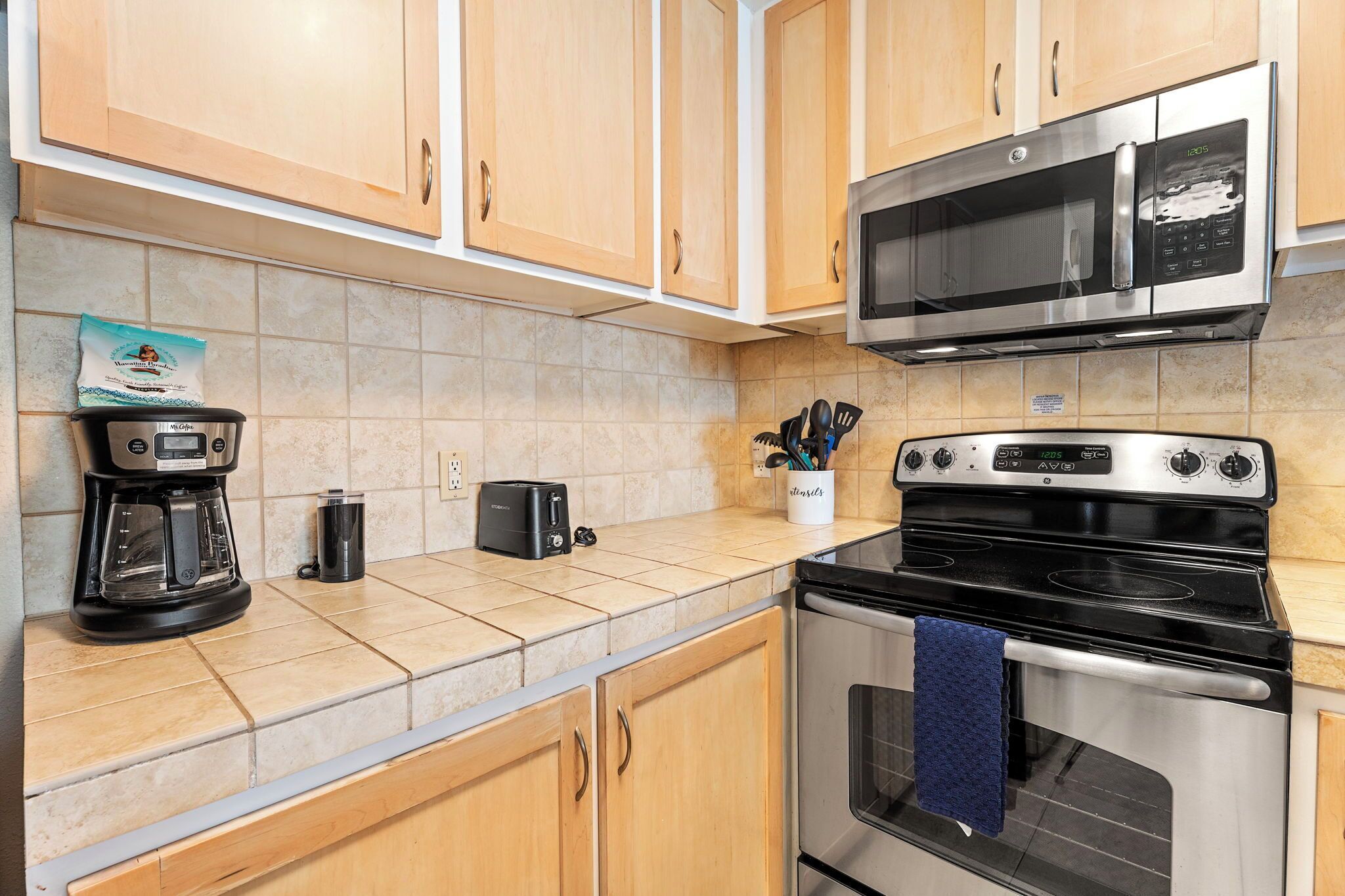 A kitchen with wooden cabinets, a stainless steel microwave, a coffee maker, a toaster, and an oven.