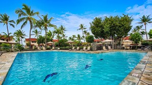 Ein Swimmingpool mit klarem, blauem Wasser, umgeben von Palmen und Liegestühlen.
