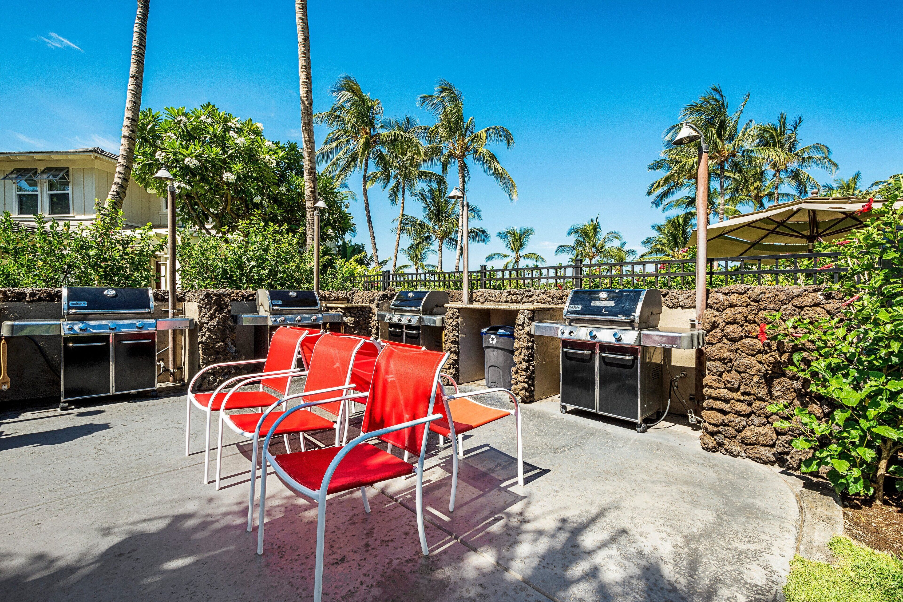 An outdoor patio with barbecue grills, red chairs, and a stone wall.
