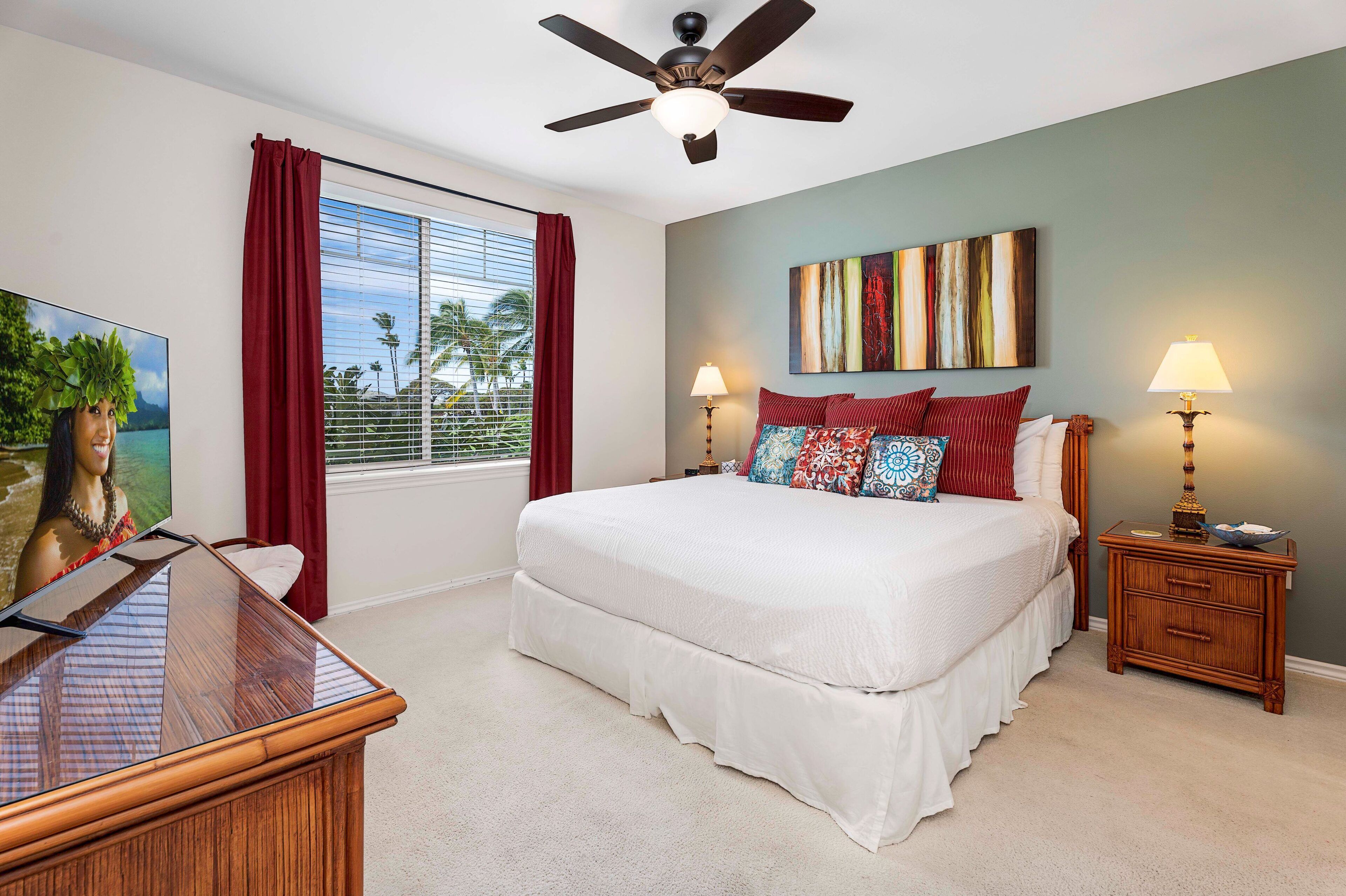 A bedroom with a bed, a ceiling fan, a TV, a window with curtains, and a painting on the wall.