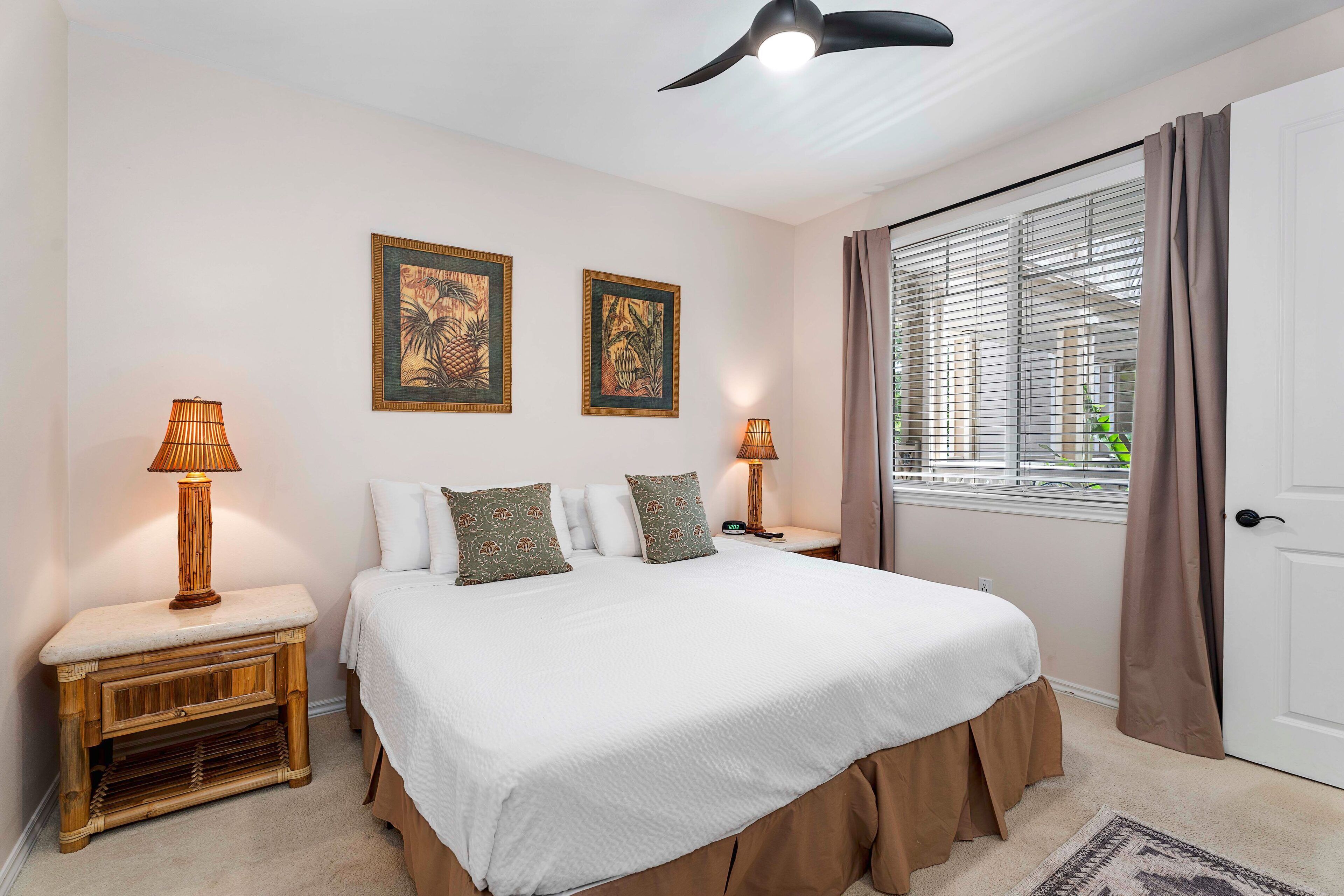 A bedroom with a bed, two bedside tables, a nightstand, a ceiling fan, and a window with curtains.