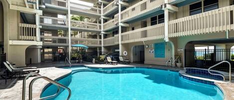 A multi-level hotel with a central swimming pool, outdoor seating, and balconies.
