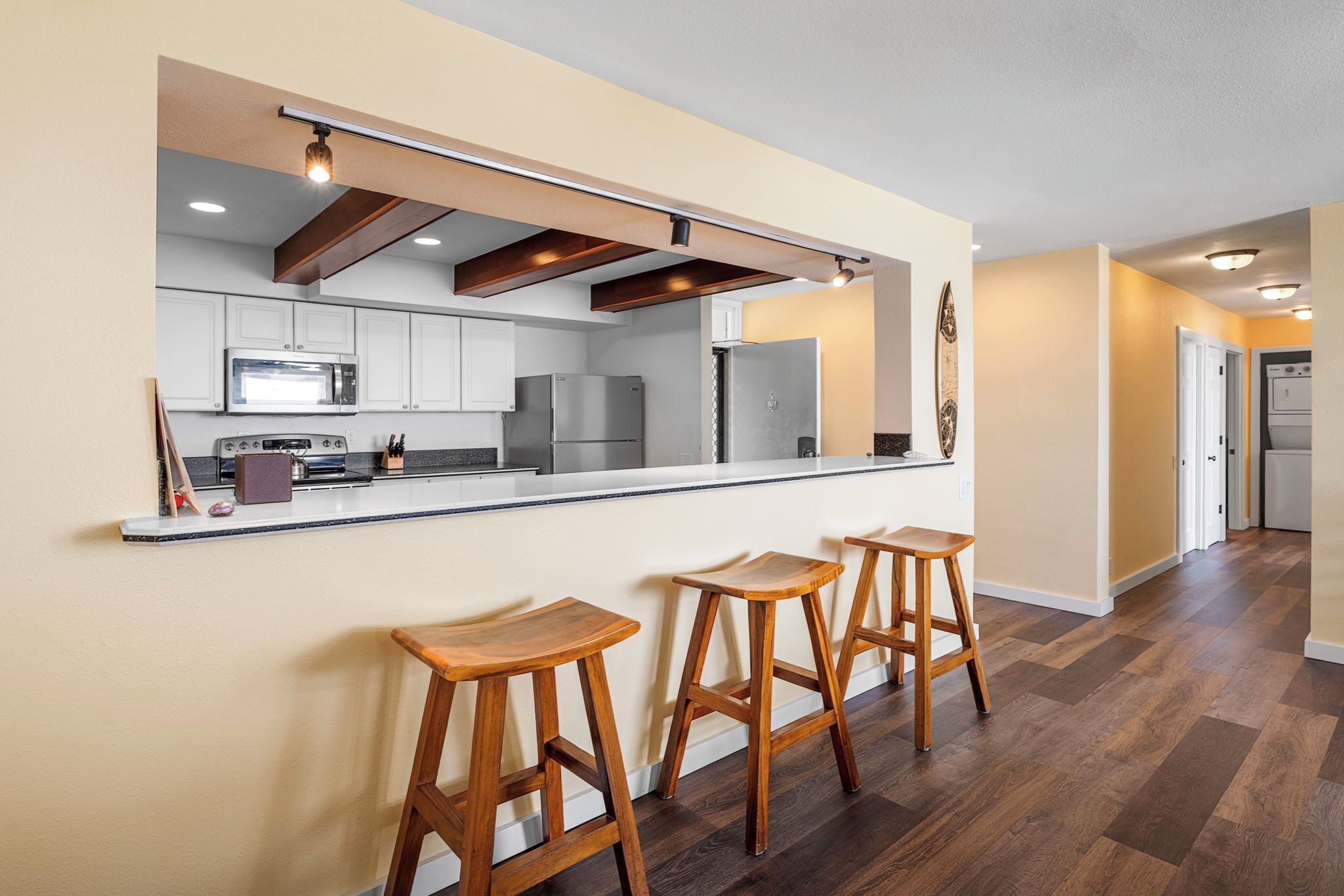 A modern kitchen with white cabinets, stainless steel appliances, and wooden bar stools.