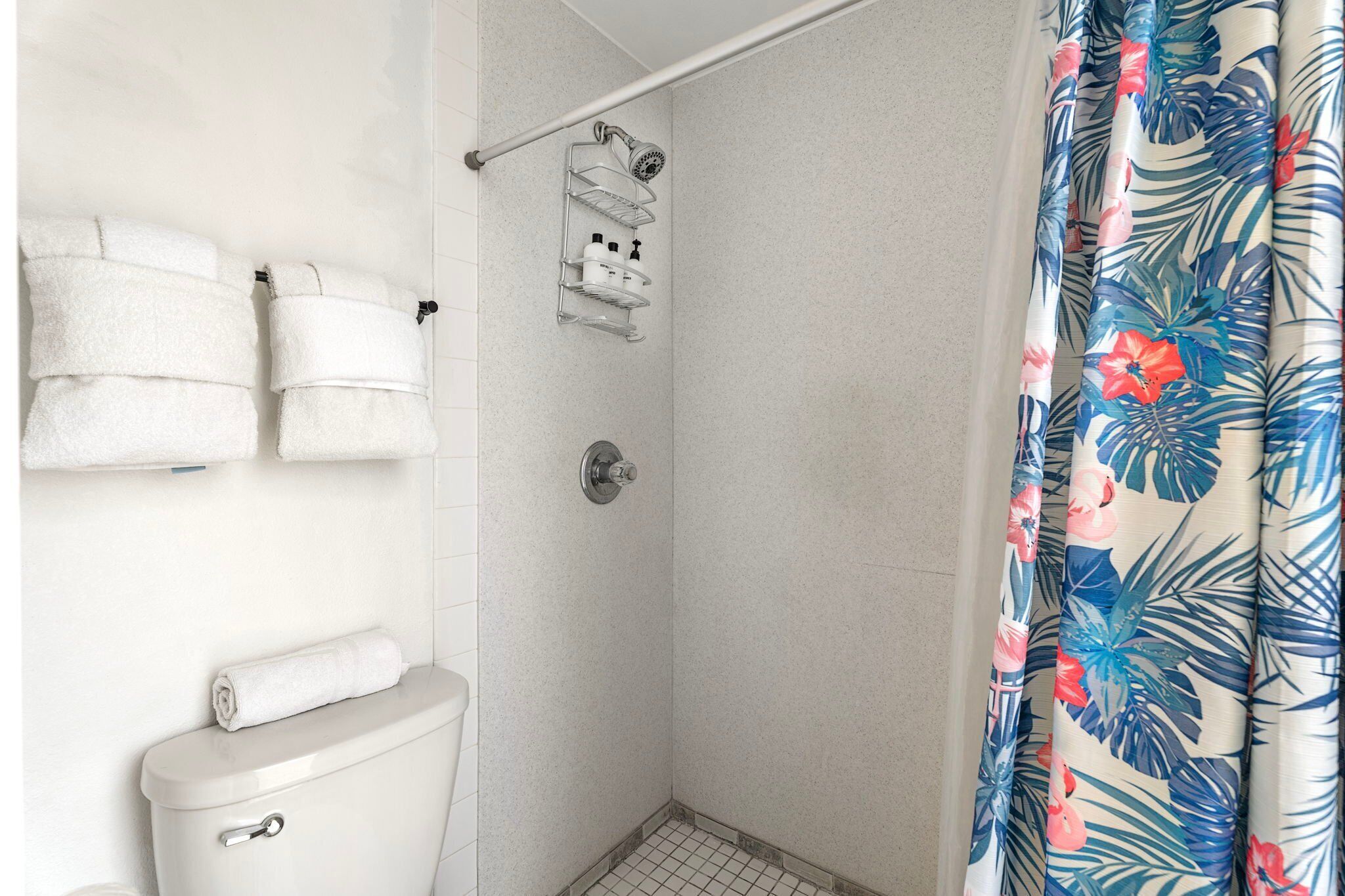 A bathroom with a shower, a toilet, and a towel rack with towels.