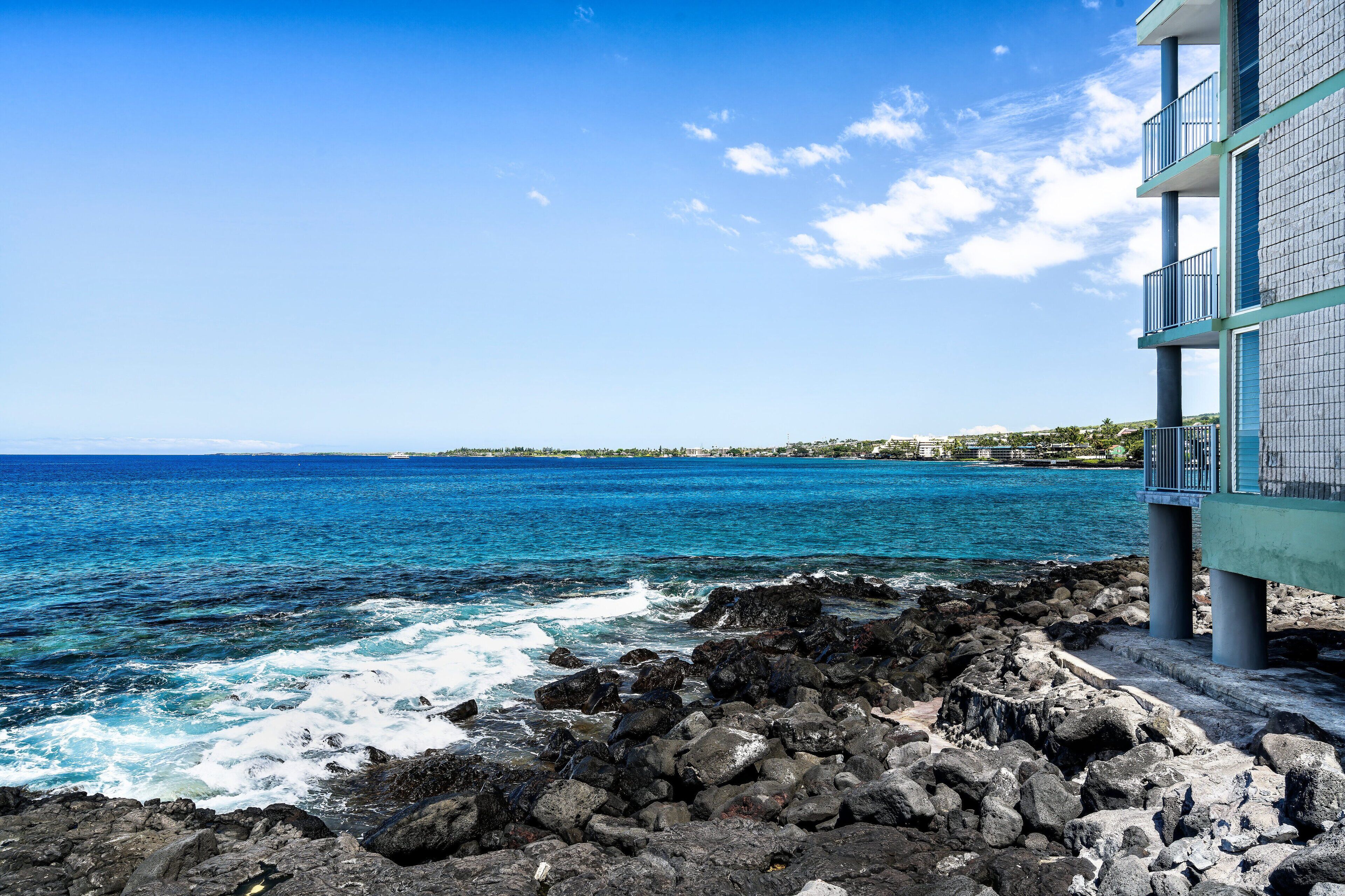 A coastal view with a rocky shoreline and a building with balconies overlooking the ocean.
