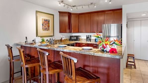 Una cocina con armarios de madera, encimera de granito, refrigerador de acero inoxidable y una barra con taburetes de madera.