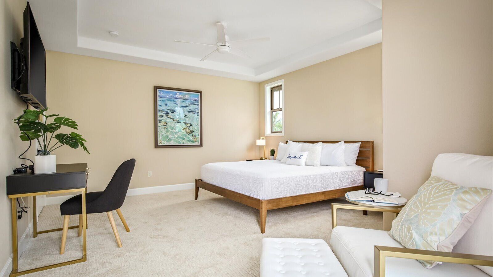 A bedroom with a bed, a desk, a chair, a bedside table, a lamp, and a plant.