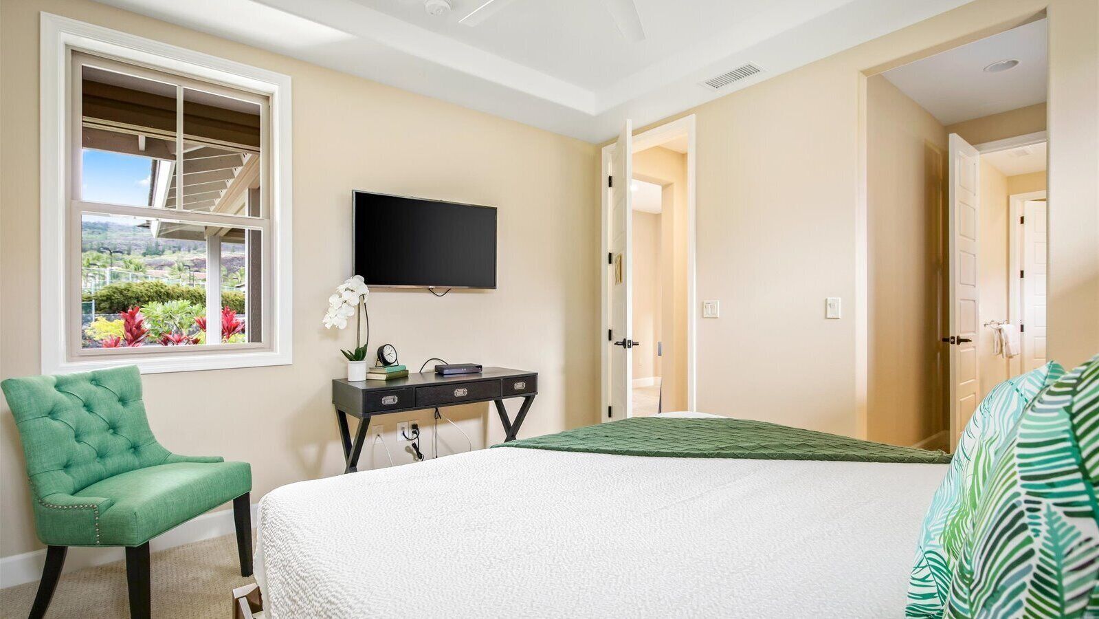 Une chambre à coucher comprenant un lit, un bureau, une chaise, un téléviseur et une fenêtre donnant sur un paysage verdoyant.