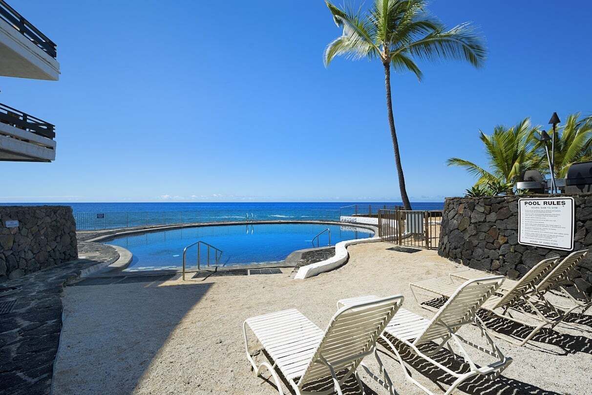 A pool area with lounge chairs, a palm tree, and a sign indicating pool rules.