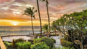A resort patio with a view of the ocean at sunset, palm trees, and outdoor seating areas. - Beautiful Ocean View - Updated - Wifi Included- Vrkcv (Kailua-Kona)