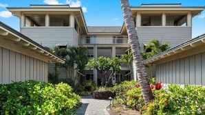 A two-story hotel with a central courtyard, surrounded by lush greenery and palm trees. - Family & Couples' Waikoloa Escape - Concierge, Pools & A-bay Beach Fun - Vrkcv (Waikoloa)