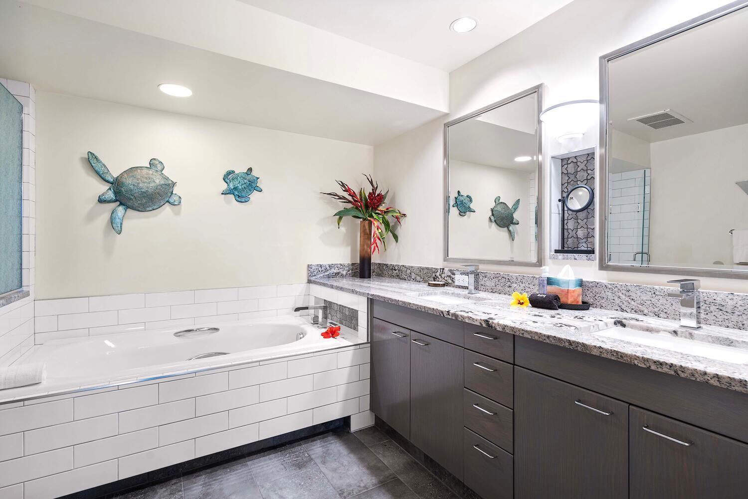 Een moderne badkamer met een groot bad, een wastafel met spiegel en decoratieve wanddecoratie van zeeschildpadden.
