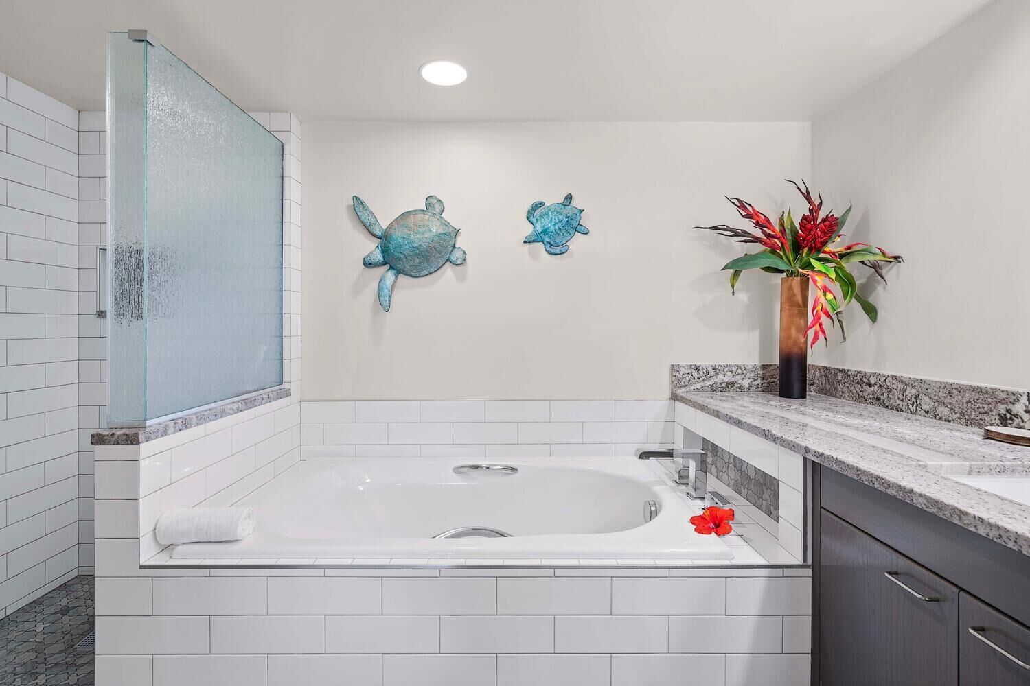 Un bagno con una vasca da bagno grande, pareti piastrellate di bianco, cabina doccia in vetro e una parete decorata con due sculture di tartarughe.