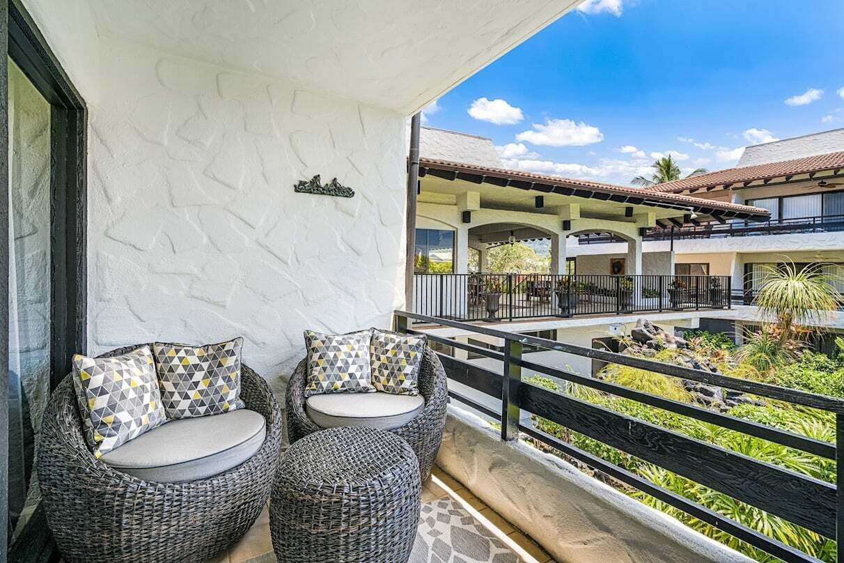A balcony with wicker furniture and a view of a building with a tiled roof.